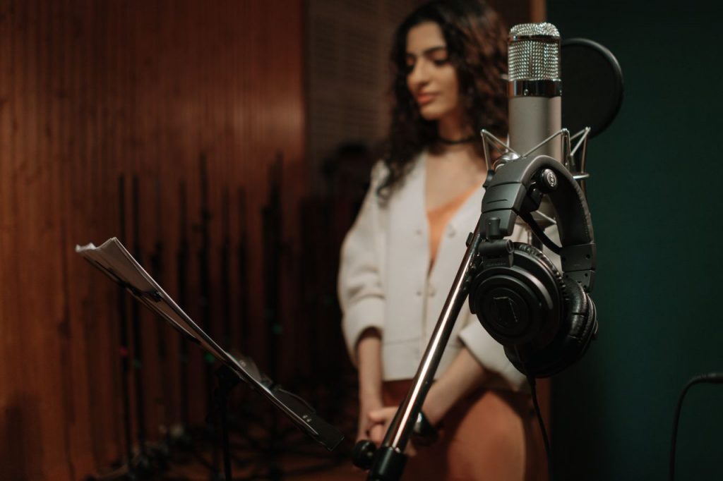 A woman stands in a recording studio, focusing on audio production with a prominent microphone.